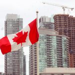 A canadian flag flying in front of some tall buildings.