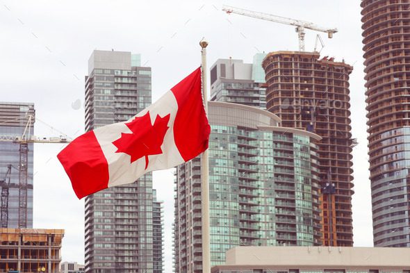 A canadian flag flying in front of some tall buildings.
