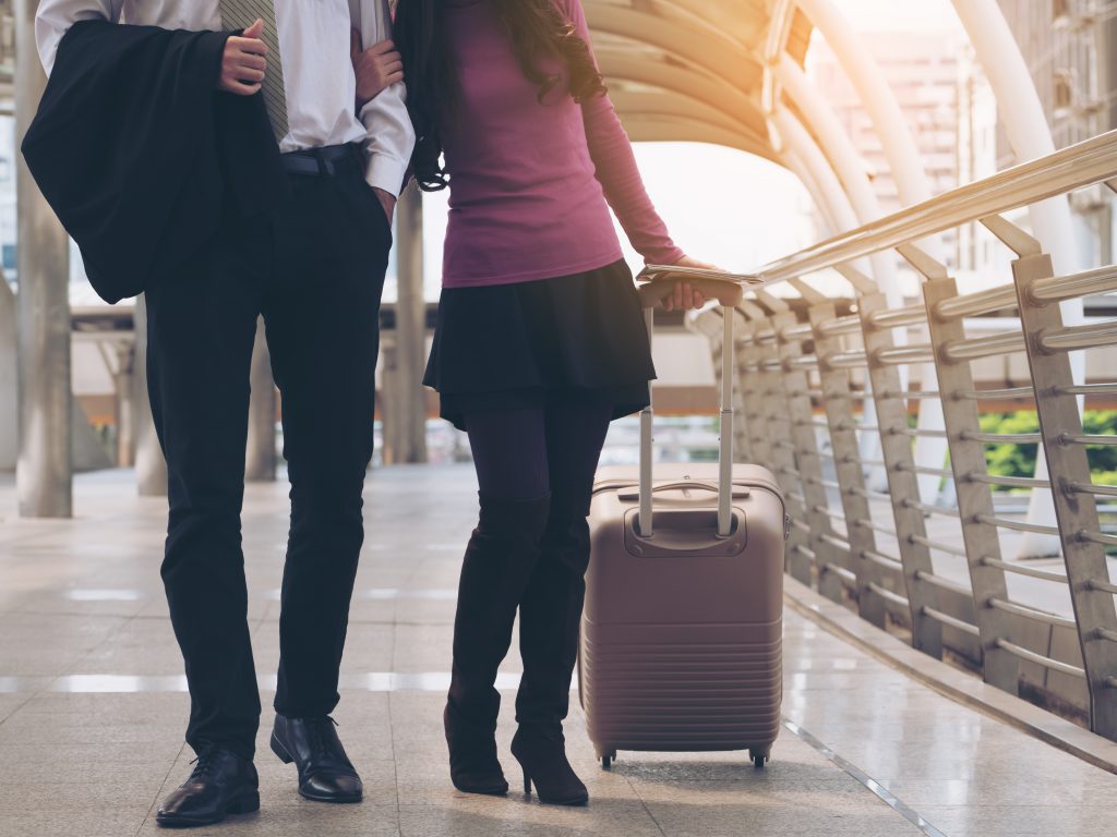 A man and woman walking with luggage on the sidewalk.