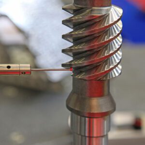 A person is using a drill to make holes in the shaft of an industrial machine.