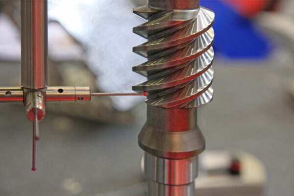 A person is using a drill to make holes in the shaft of an industrial machine.