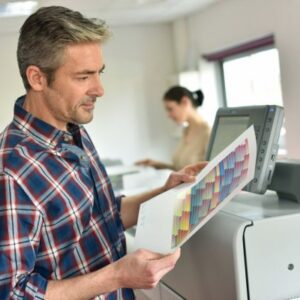 A man holding papers standing next to an open printer.