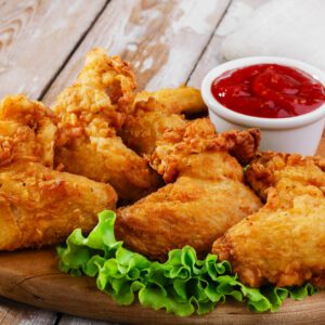 A wooden platter of fried chicken and ketchup.