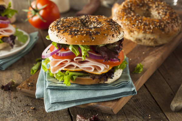 A sandwich with meat, lettuce and tomato on a bagel.