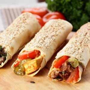 Three burritos are sitting on a table with vegetables.