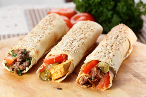 Three burritos are sitting on a table with vegetables.