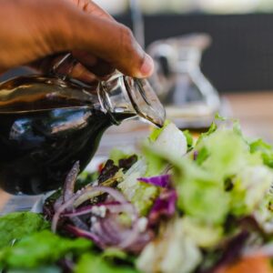 A person pouring oil on salad.