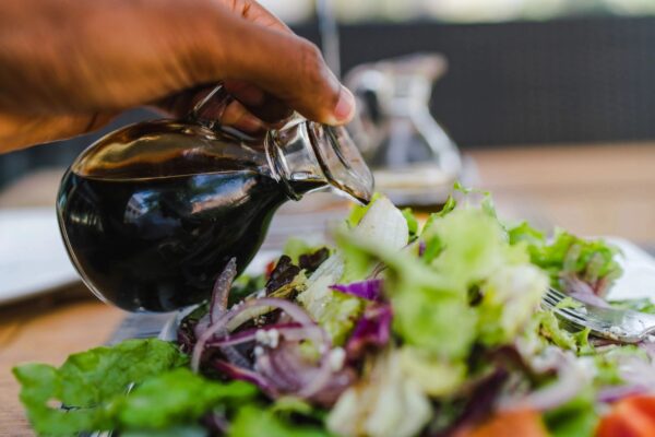 A person pouring oil on salad.