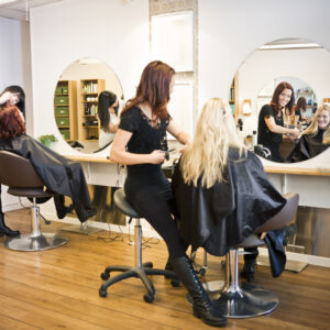 A woman sitting in front of a mirror while another person sits at the hair dresser.