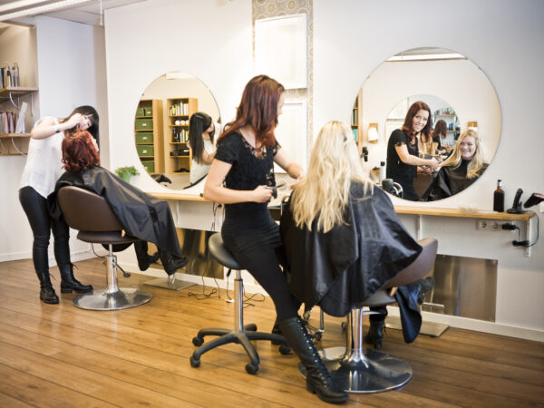 A woman sitting in front of a mirror while another person sits at the hair dresser.